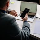 Man in office using smartphone and laptop, showing time management.